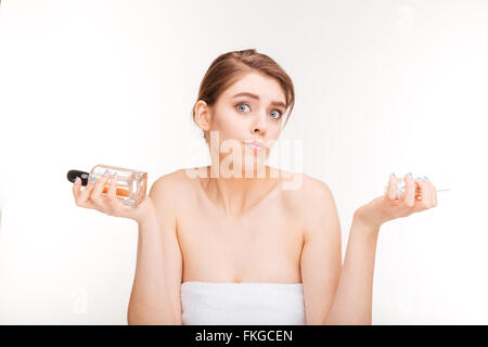 Portrait of young woman choosing confus entre deux parfums sur fond blanc Banque D'Images