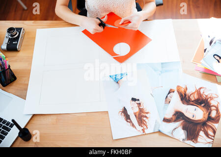 Vue de dessus de table des femme photographe faire collage avec photos à l'aide de ciseaux dans l'office Banque D'Images