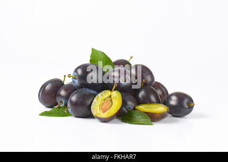 Tas de prunes mûres avec des feuilles sur fond blanc Banque D'Images