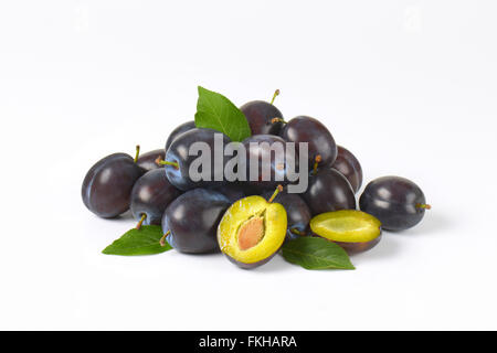 Tas de prunes mûres avec des feuilles sur fond blanc Banque D'Images