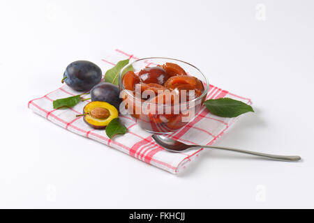 Prunes fraîches et le bol de conserves de prunes sur torchon à carreaux Banque D'Images