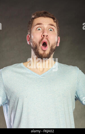 Portrait de choqué étonné surpris bel homme en chemise. Jeune homme posing in studio sur noir. Banque D'Images