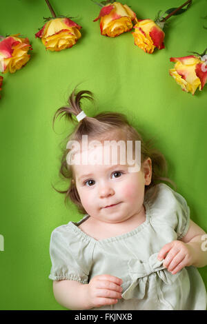 Jolie petite fille couchée sur une couverture verte avec des roses jaunes Banque D'Images