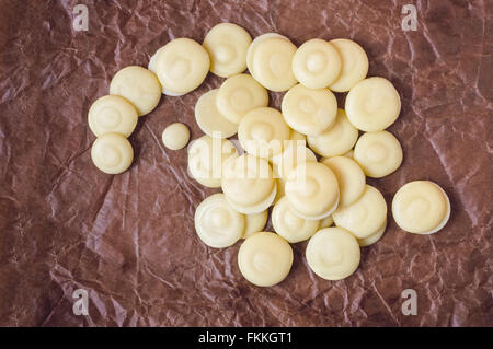 Vue de dessus du beurre de cacao biologique des boutons sur un papier parchemin froissé marron texturée. Banque D'Images