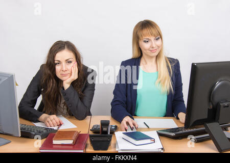 La situation dans le bureau - une femme assise à une table dans la frustration, l'autre un plaisir de regarder un écran d'ordinateur Banque D'Images