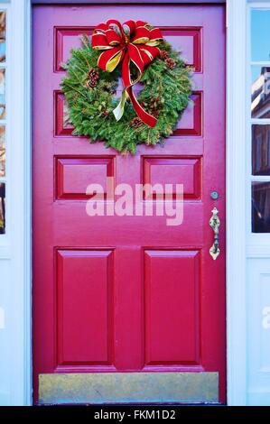 Vacances de Noël la couronne de pin avec cocottes et arc rouge sur une porte rouge Banque D'Images