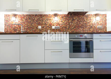 Maison moderne cuisine avec armoires, acier inoxydable four blanc, mosaïque sur le mur, petites lumières Banque D'Images