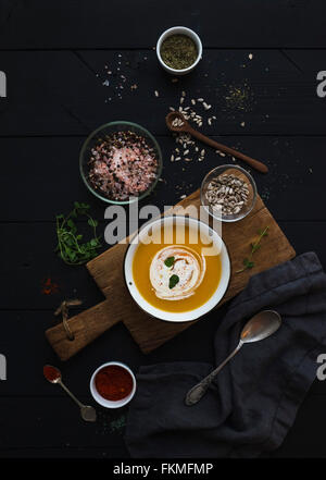 Soupe de potiron à la crème, les graines et les épices dans un bol en métal rustique sur planche de bois plus grunge fond noir. Vue d'en haut Banque D'Images