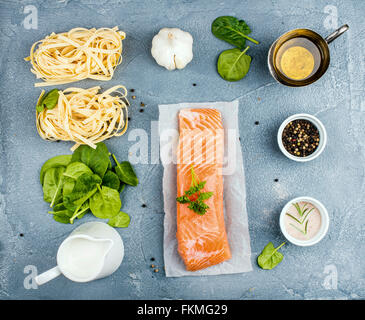 Ingrédients pour la cuisson des pâtes tagliatelles au saumon, épinards et crème sur fond texturé de béton gris, vue du dessus Banque D'Images