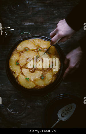 Une femme est de trancher un gâteau d'ananas est photographié par le haut.