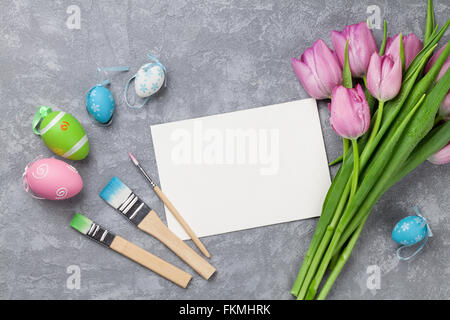 Les oeufs de Pâques colorés, tulipes et carte sur table en pierre. Top View with copy space Banque D'Images