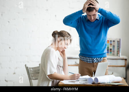 Portrait de deux collaborateurs faisant valoir au travail, ayant à lutter contre un bureau moderne. Les jeunes ont souligné l'homme tenait la tête dans les mains en consternation Banque D'Images