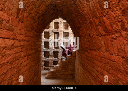 Un jeune moine lire avec la lumière du soleil dans les temples de Bagan, Myanmar Banque D'Images