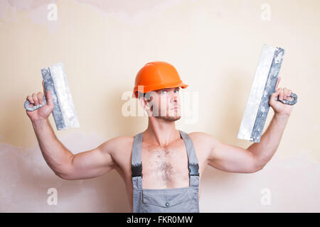 Un homme en bleu de travail et casque avec deux spatules dans la main Banque D'Images