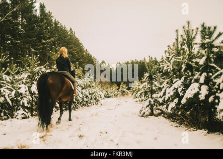 Caucasian woman riding horse on snowy path Banque D'Images