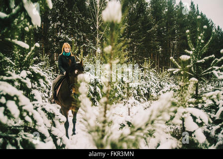 Caucasian woman riding horse in snowy forest Banque D'Images