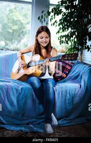 Mixed Race woman playing guitar on sofa Banque D'Images