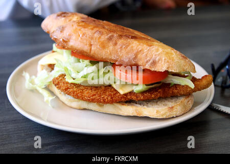 Escalope de poulet burger sur une plaque blanche à l'arrière-plan en bois Banque D'Images