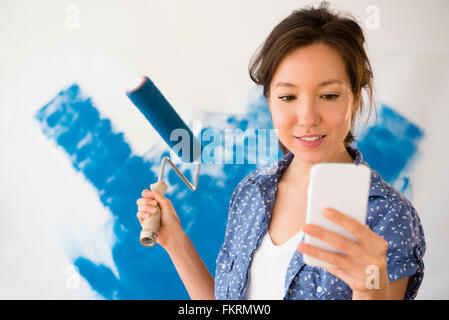 Mixed Race woman using cell phone and painting wall Banque D'Images