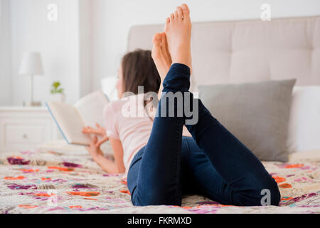 Mixed Race woman reading book on bed Banque D'Images