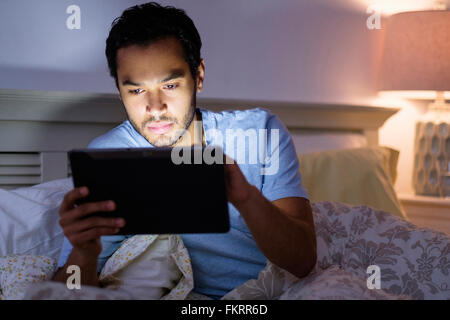 Hispanic man using digital tablet in bed Banque D'Images