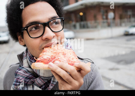 Mixed Race man eating pizza outdoors Banque D'Images