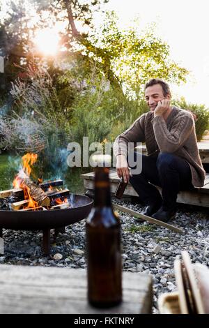 Young par feu de camp avec de la bière, de détente Banque D'Images