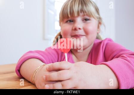 Portrait overweight girl holding heart shape lollipop Banque D'Images