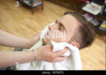 High angle vue latérale du jeune homme dans un barbier, tête en arrière, les yeux fermés après avoir séché face avec serviette Banque D'Images