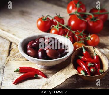 Olives noires, piment rouge et des tomates dans un bol et louche en bois rustique Banque D'Images