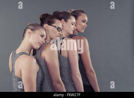 Les jeunes femmes dans une rangée, s'appuyant sur l'autre, fond gris Banque D'Images