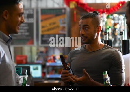 Jeune homme en public house holding Beer bottle parler à un ami Banque D'Images