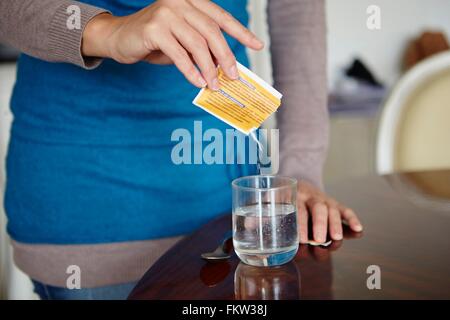 Jeune femme de mélanger des médicaments hydrosolubles du sachet-dose, en verre de l'eau Banque D'Images