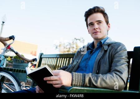 Young man reading book on park bench Banque D'Images