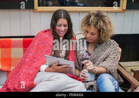 Deux amies using digital tablet on cabin porch Banque D'Images