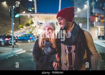 Couple smiling, marcher sur la rue au crépuscule Banque D'Images