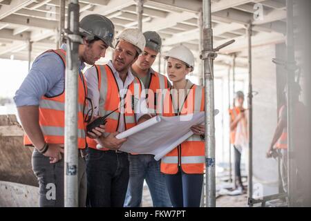 Quatre hommes et des constructeurs avec le plan on construction site Banque D'Images