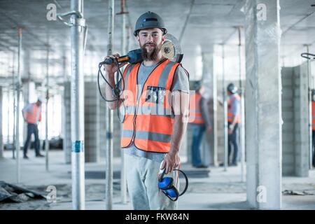 Portrait de jeune homme builder scie circulaire portant sur l'épaule on construction site Banque D'Images