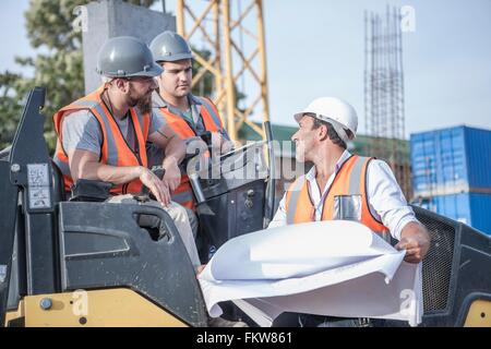 Gestionnaire du site parler avec rouleau compresseur les conducteurs sur plan directeur de site de construction Banque D'Images