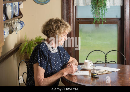 Dans une scène historique des années 1930 ou 1940, une jolie femme âgée a écrit une lettre qu'elle s'assoit à une table par une fenêtre. Banque D'Images