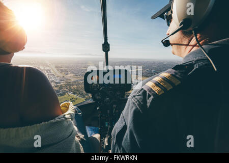 Vue arrière de deux pilotes aux commandes d'un hélicoptère le jour ensoleillé. Gros plan des pilotes assis dans le cockpit avec un soleil éclatant. Banque D'Images