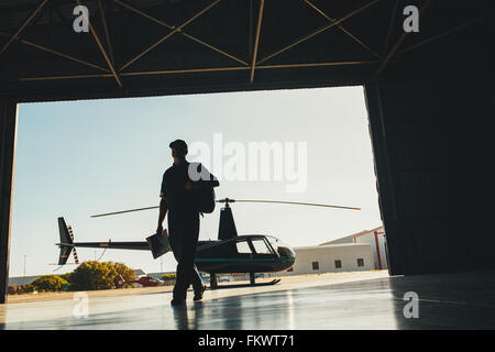 Silhouette d'un projet pilote d'arriver à l'aéroport avec un hélicoptère en arrière-plan. Le pilote d'hélicoptère dans le hangar de l'avion. Banque D'Images