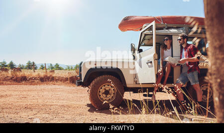 Jeune couple avec car on road trip reading map pour les directions. Jeune homme et femme prendre pause dans le voyage. Banque D'Images