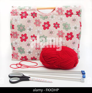 Tricot à motifs fleurs rose / artisanat sac avec des aiguilles à tricoter, laine rouge et ciseaux sur un fond blanc. Banque D'Images