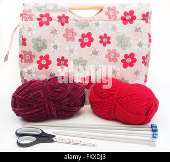 Tricot à motifs fleurs rose / artisanat sac avec des aiguilles à tricoter, laine rouge et bourgogne et ciseaux sur un fond blanc. Banque D'Images