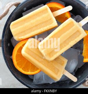 Sucettes glacées au yogourt orange congelé close up dans un seau en étain rempli de glace rustique avec des tranches de fruits frais Banque D'Images