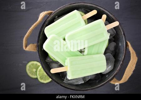 Sucettes glacées au yogourt lime fait maison dans un cadre rustique rempli de glace seau en étain contre un arrière-plan en ardoise Banque D'Images