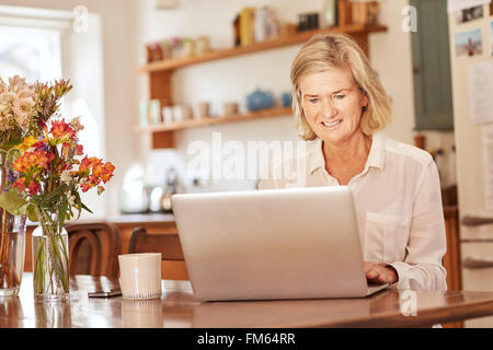 Hauts femme travaillant sur un ordinateur portable dans sa cuisine Banque D'Images