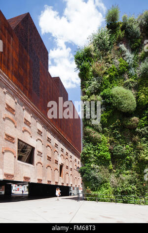 La vue latérale d'un bâtiment appelé La Caixa Forum, à Madrid, avec la conception inhabituelle, comme une dame passe entre elle et un mur de plantes à côté. Banque D'Images