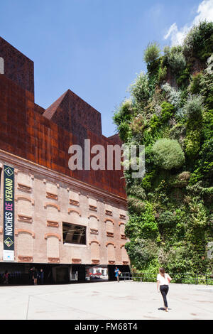 La vue latérale d'un bâtiment appelé La Caixa Forum, à Madrid, avec la conception inhabituelle, comme mesdames passe entre elle et un mur de plantes à côté. Banque D'Images